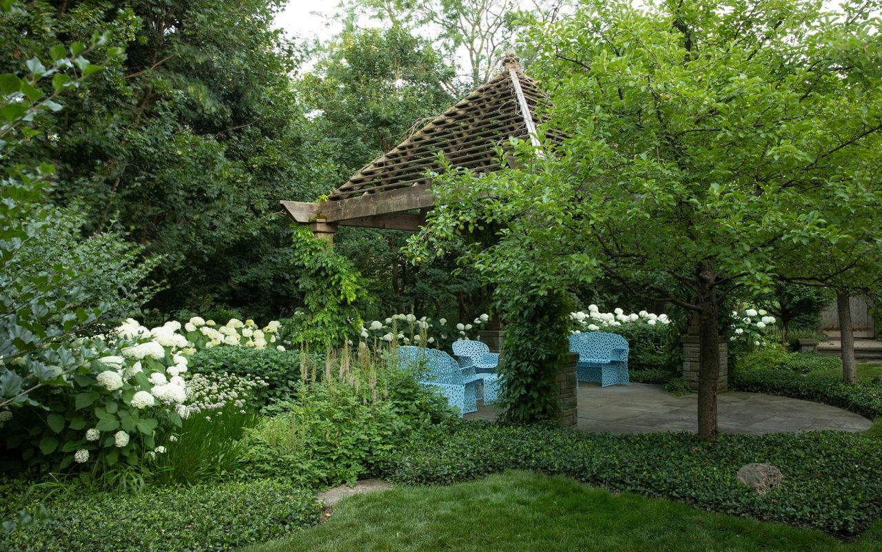 Wood pergola with a peaked roof and bluestone paving set within a garden.