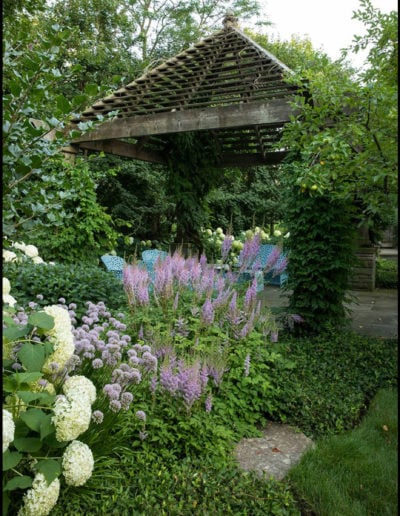 Pérgola de madera con techo a dos aguas situada en un jardín de plantas perennes mixtas.