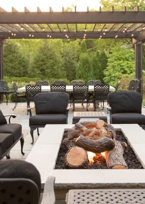 Modern wood and steel pergola with dining table set overlookingModern wood and steel pergola and raised fire pit with faux logs and casual seating. the backyard garden.