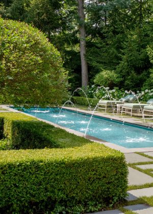 Pool with arching water feature nestled in a stone stepper deck with lounge chairs and hydrangeas