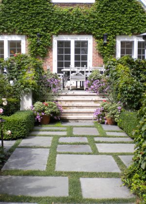 Elevated terrace by pool with boxwood hedges surrounded by lush, vibrant, annual plantings