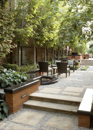 Flagstone steppers embedded in gravel with multiple seating areas and water feature all bordered by a brick and marble wall