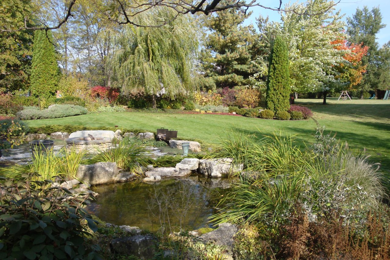 Pond with fire pit in background, mowed lawn surrounded by flower beds