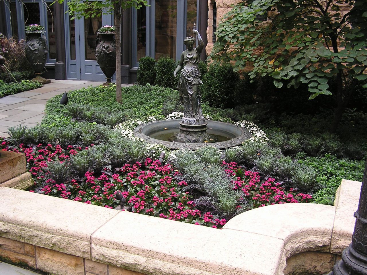 Grecian fountain statue surrounded by annual and ground cover bed