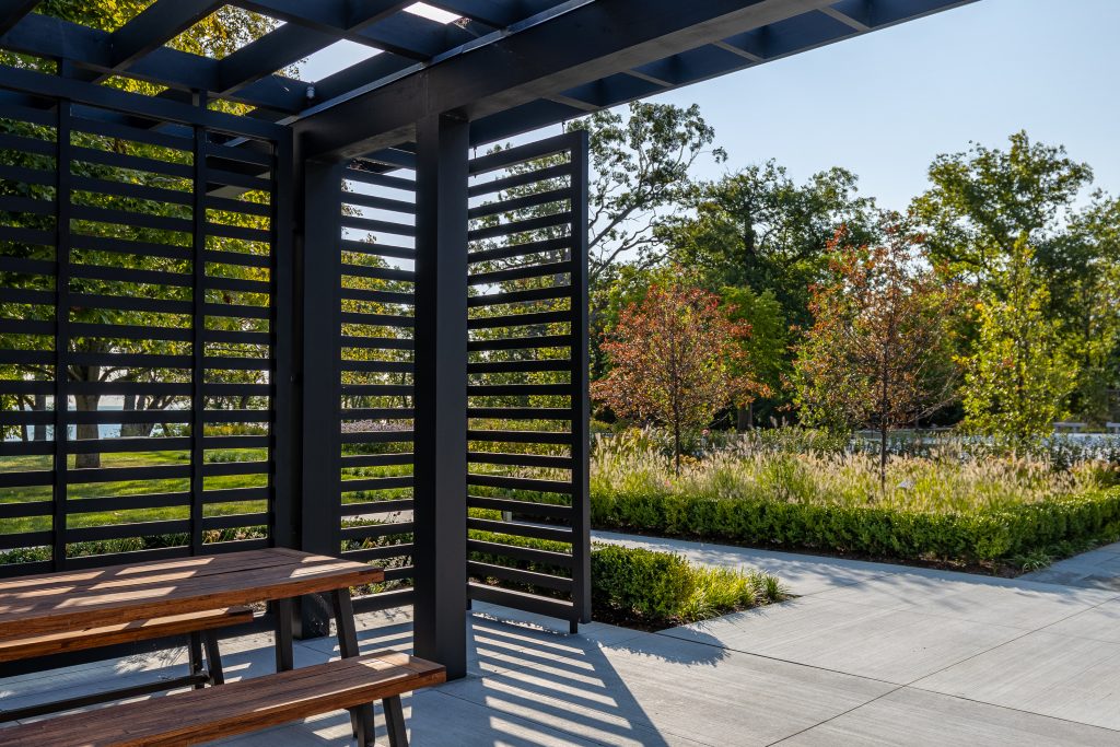 Sucá metálica interior con banco, bojes, terraza de piedra azul y vegetación natural